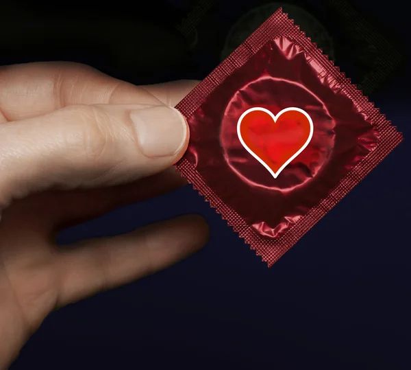 Man's hand with a red condom pack and heart symbol on it — Stock Photo, Image