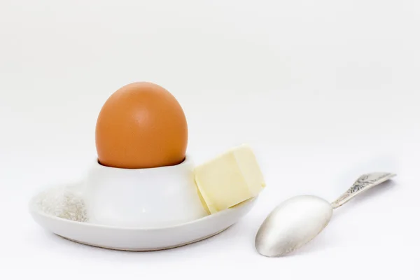 Белый яичный стакан с коричневым яйцом, ложкой и маслом с солью — стоковое фото