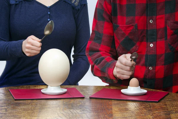 Woman and man with spoons eating hen and ostrich eggs — Stock Photo, Image