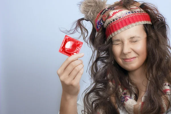 Girl with a knitted hat and a red condom pack in the hand — Stock Photo, Image