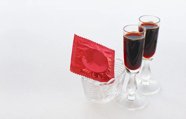 Red condom in a small vase and two glasses with a dark drink — Stock Photo, Image