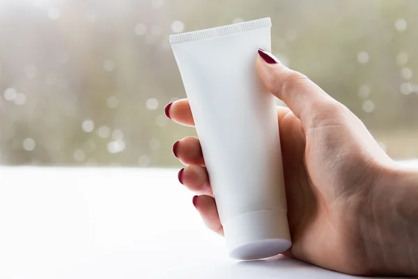 Mano donna con un tubo bianco crema — Foto Stock