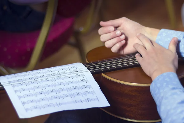 Young male's hands and guitar with musical scores — Stockfoto