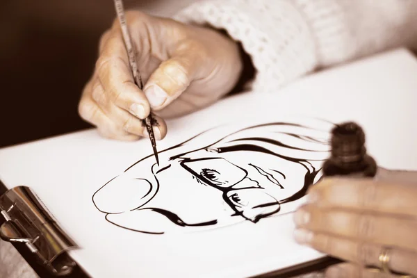 Female's hands drawing a caricature with black ink — Stock Photo, Image