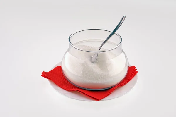 Сахар в стеклянной миске с ложкой на блюдце с красной салфеткой — стоковое фото