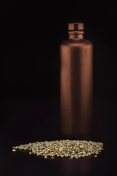 Bronze-colored ceramic bottle and hemp seeds — Stock Photo, Image