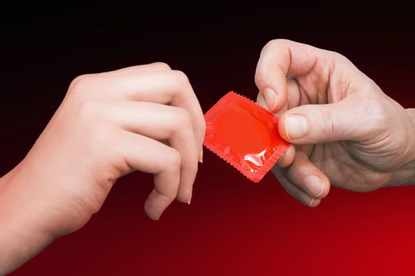 Man's hand giving woman's hand a red  condom — Stock Photo, Image