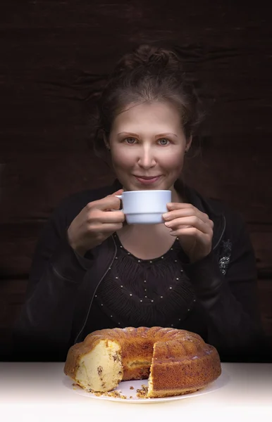 Joven mujer sonriente bebiendo café y un pastel en una mesa — Foto de Stock