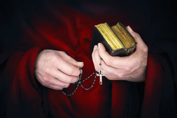 Monge misterioso com uma capa segurando bíblias e um rosário preto — Fotografia de Stock