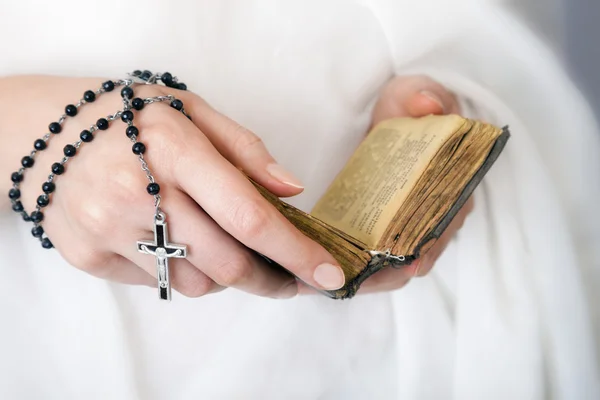 Handen van de jonge vrouw met een rozenkrans en een Bijbel — Stockfoto