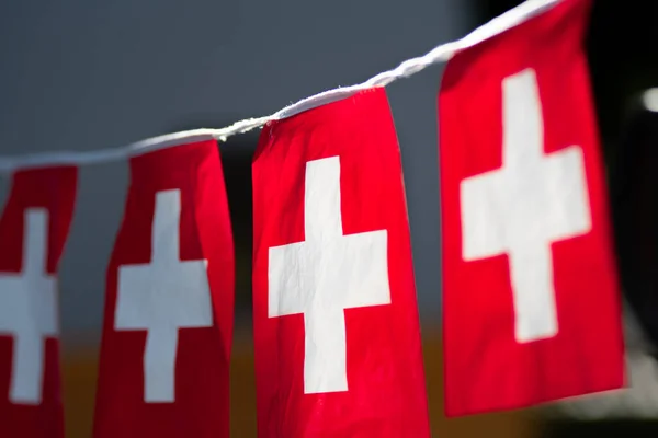 String banner of small swiss Switzerland Red and White Cross flags hanging up with a close-up perspective with blurred background and copy space.