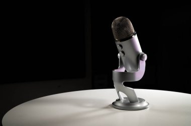 Gri gri USB yoğunlaştırıcı mikrofon ayarlanabilir masa üstü standı ile koyu renkli bir kontrast odasında beyaz bir masanın üzerinde duruyor.