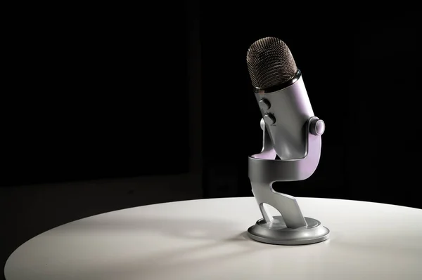 Gri gri USB yoğunlaştırıcı mikrofon ayarlanabilir masa üstü standı ile koyu renkli bir kontrast odasında beyaz bir masanın üzerinde duruyor.