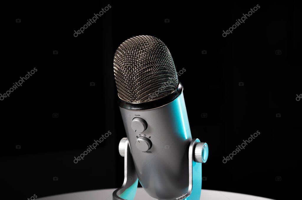 Silver grey USB condenser microphone with adjustable tabletop stand sitting on a white table in a dark contrast room with a neon cyan highlight shine color pop with copy space