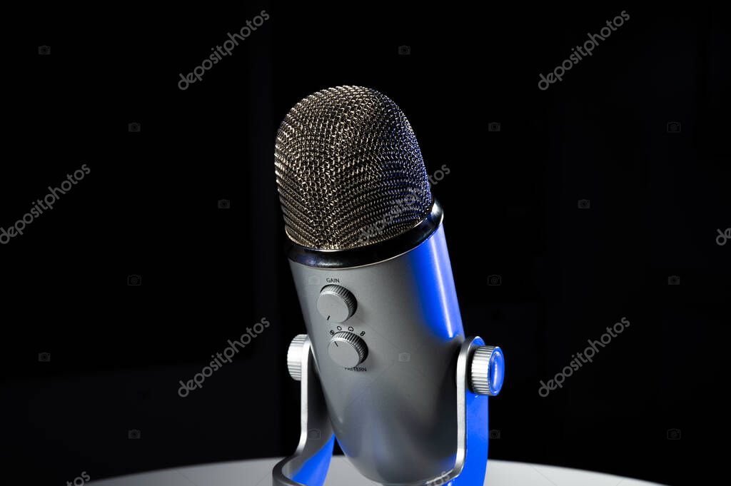 Silver grey USB condenser microphone with adjustable tabletop stand sitting on a white table in a dark contrast room with a neon blue highlight shine color pop with copy space