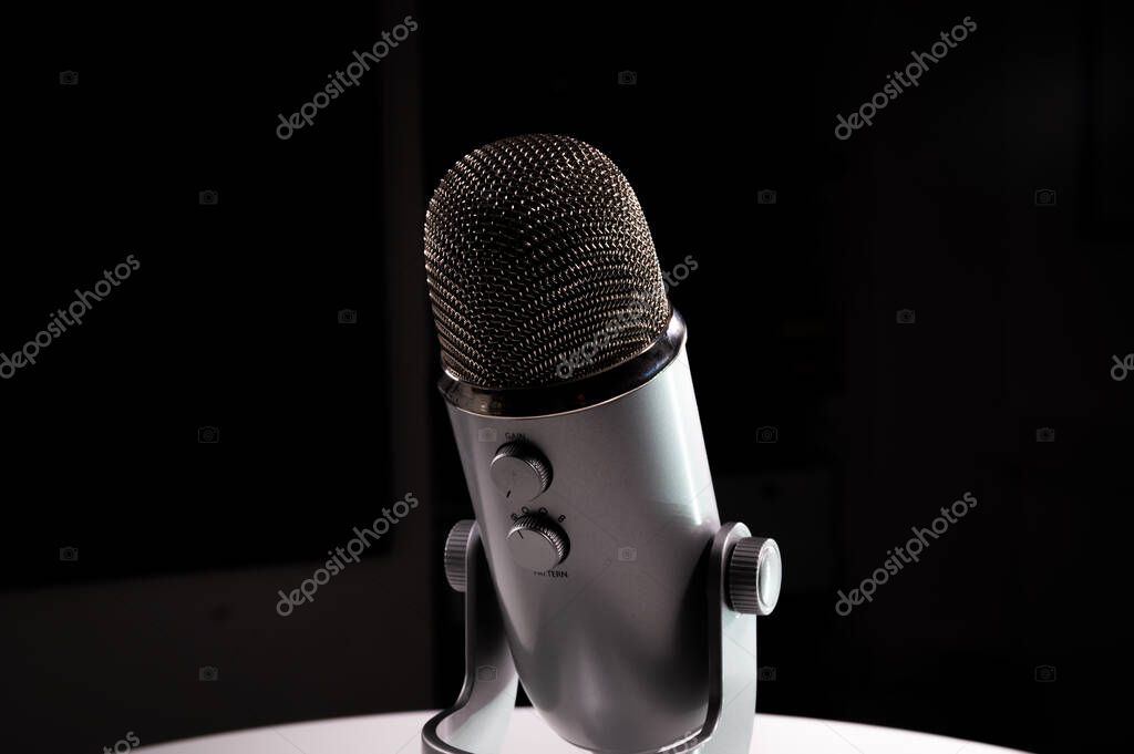 Silver grey USB condenser microphone with adjustable tabletop stand sitting on a white table in a dark contrast room with a neon highlight shine pop with copy space