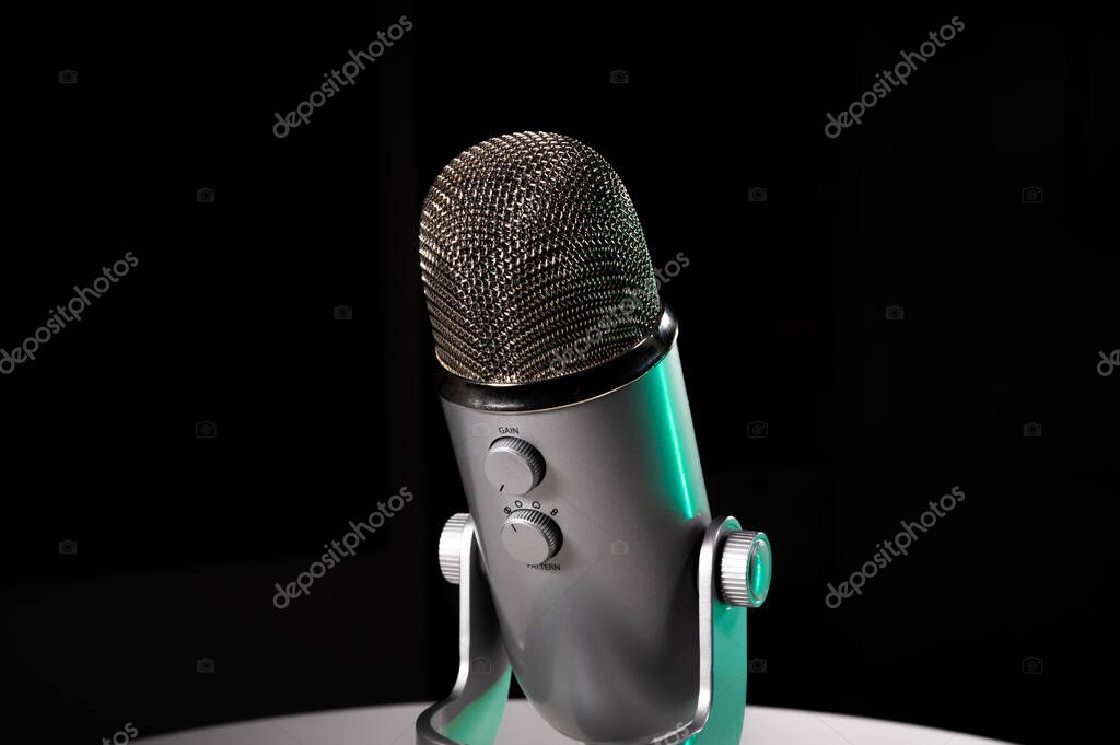 Silver grey USB condenser microphone with adjustable tabletop stand sitting on a white table in a dark contrast room with a neon teal highlight shine color pop with copy space