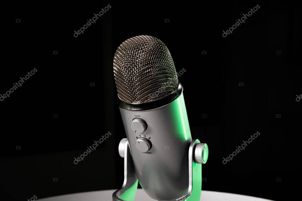 Silver grey USB condenser microphone with adjustable tabletop stand sitting on a white table in a dark contrast room with a neon lime green highlight shine color pop with copy space