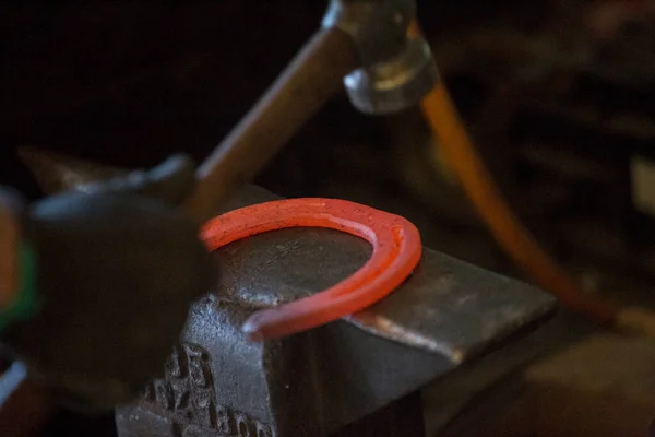 Hard work in the smithy on the anvil. Hammering glowing steel horse shoe. Blacksmith forges a hot horseshoe