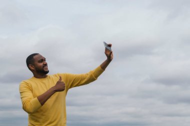 Genç siyah bir adam fotoğraf çekiyor ve kameraya gülümsüyor.