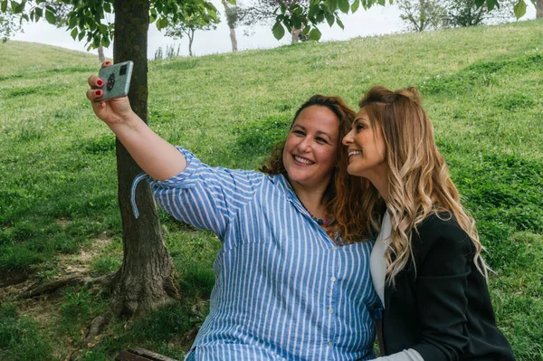 Parkta cep telefonuyla selfie çeken iki güzel arkadaş.