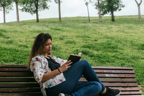 Parktaki bankta kitap okuyan güzel bir genç kız.