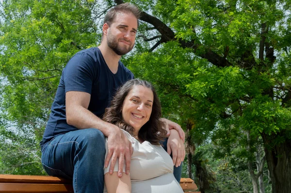 怀孕的夫妇坐在长椅上 在公园里摆姿势 — 图库照片