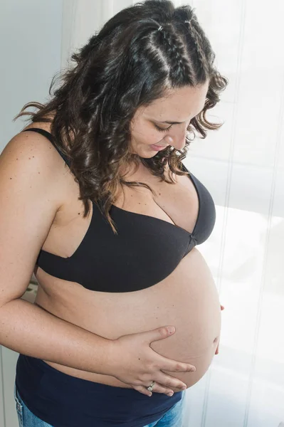怀孕的女人看着窗外 摸着肚子 — 图库照片