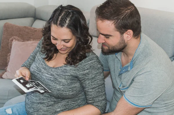 Pregnant couple looking at an ultrasound of their future child, smiling and very happy