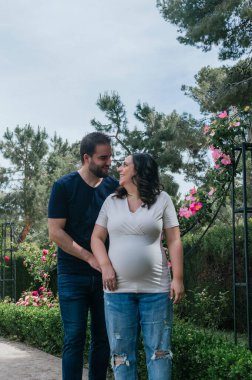 Hamile çift parkta yürüyor ve poz veriyor.