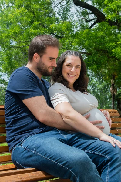 怀孕的夫妇坐在长椅上 在公园里摆姿势 — 图库照片