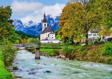 St. Sebastian 'ın sembolik kilisesi, büyüleyici bir cadde ve sonbahar renkli ağaçlar tarafından çerçevelenmiş, doğrudan Ramsauer Ache nehrinden görülüyor. Ramsau bei Berchtesgaden, Almanya