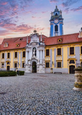 Durnstein Manastırı 'nın tarihi kaldırım taşı avlusu ve süslü portalının dikey çekimi Vaçu Vadisi Avusturya' sında pembe ve mor bir günbatımı gökyüzü tarafından aydınlatılmıştır.