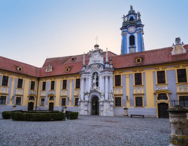 Durnstein Manastırı 'nın barışçıl parke avlusunun geniş yatay manzarası. Avusturya' da açık bir alacakaranlık gökyüzüne karşı barok beyaz kapı ve mavi kule var.