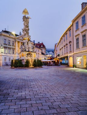 Avusturya 'da alacakaranlıkta Kutsal Üçlü Sütun ve tarihi Rathaus' un (belediye binasının) yer aldığı Baden bei Wien Meydanı 'nın ana meydanındaki şenlikli Noel pazarının dikey görüntüsü