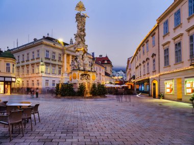 Avusturya 'da alacakaranlıkta tarihi Rathaus (belediye binası) ve Kutsal Üçlü Sütun' un yer aldığı Baden Bei Wien Meydanı 'nın ana meydanındaki şenlikli Noel pazarının yatay görüntüsü