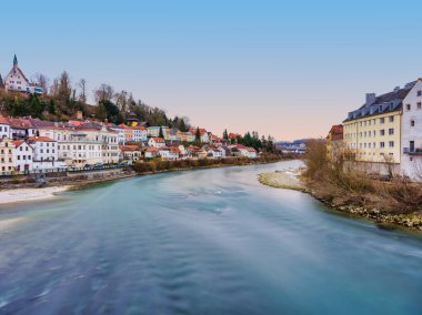 Avusturya 'nın Steyr kentindeki nehir kenarındaki renkli tarihi evlere bakan ipeksi Enns Nehri üzerindeki bir köprüden çekilen uzun pozlu bir fotoğraf, alacakaranlıktaki mavi saatte..