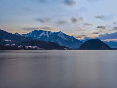 Avusturya 'da dramatik bulutlu bir gündoğumu sırasında karla kaplı Salzkammergut dağlarıyla çevrili Wolfgang Gölü' nün (Wolfgangsee) geniş açılı görüntüsü