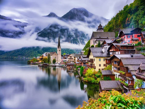 Avusturya 'daki dağ sisinin altındaki gölün ipeksi yumuşak sularına yansıyan Hallstatt' ın dik dağ yamacına tünemiş geleneksel evlerin uzun pozlu manzarası