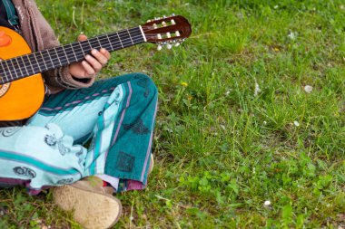 Sakallı ve gözlüklü hippi çimlerin üzerinde gitar çalıyor.