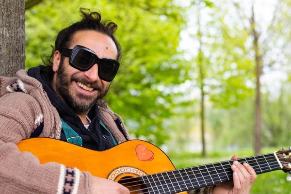 Hippy hombre con barba y gafas tocando la guitarra al aire libre en la hierba —  Fotos de Stock