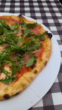 Siyah beyaz kareler üzerinde Prosciuto e rogula pizza.