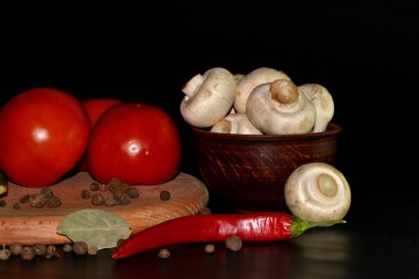 Kırmızı domatesler, mantarlar, tabakta kırmızı biber, hepsi yuvarlak ahşap tahta üzerinde koyu arkaplan