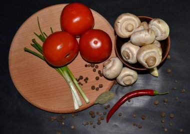 Kırmızı domates, mantar, sarımsak, kırmızı acı biber, koyu arkaplanda yuvarlak tahta üzerinde yeşil soğan. Üst görünüm