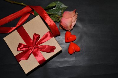 Kırmızı fiyonklu bir hediye kutusu, pembe gül ve koyu aromalı mumlar. Üst görünüm