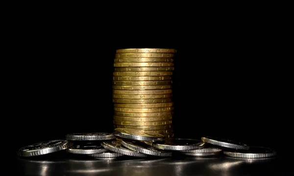 Stack of golden coins and heap of silver coins on black background