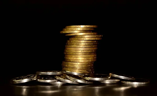 Stack of golden coins and heap of silver coins on black background. Concept of saving money