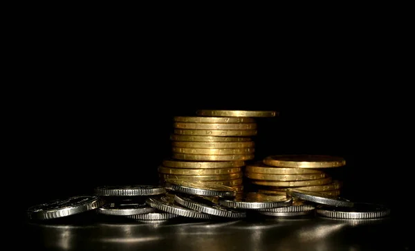 Stack of golden coins and heap of silver coins on black background