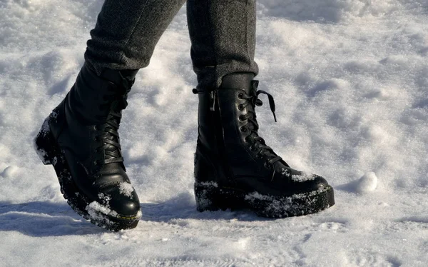 Woman's legs in high black boots walking down the street in the snow