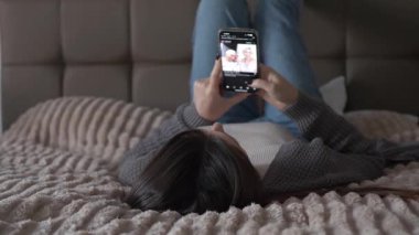 Yatağında uzanmış, akıllı telefonuyla sosyal medyada gezinen genç bir kadın. Sakin ve rahat bir atmosfer, doğal gün ışığı ve tarafsız bir ruh hali. Günlük dijital rutinin konforlu ev hayatı anı